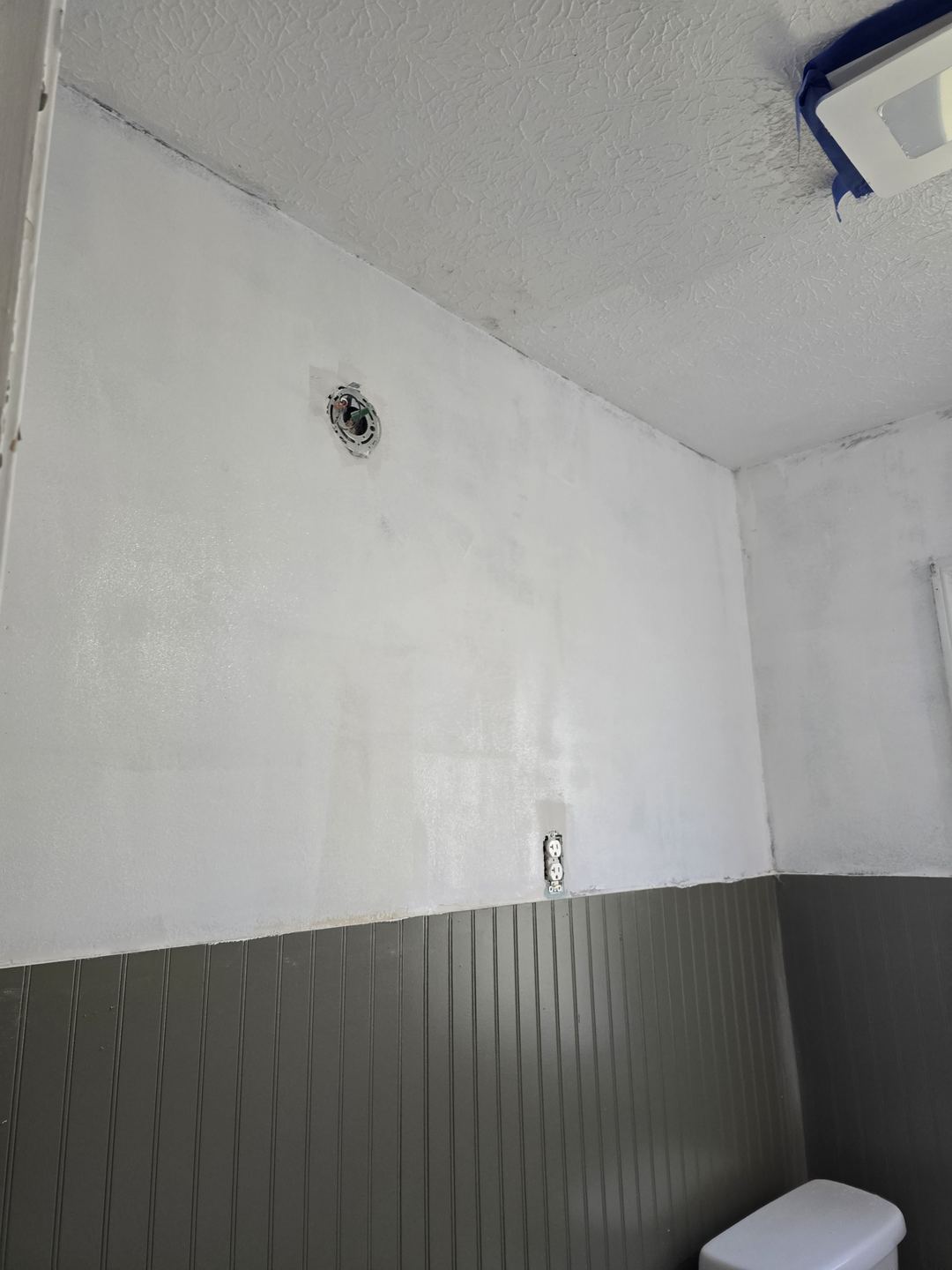 The same bathroom walls skim-coated smooth and primed white above dark green beadboard