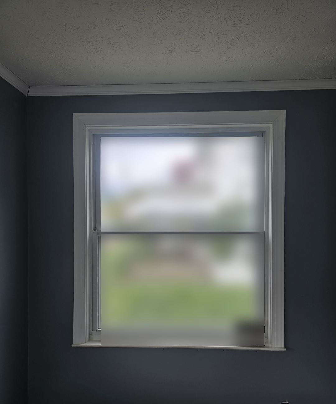 Bedroom wall painted slate blue around a double-hung window with white trim